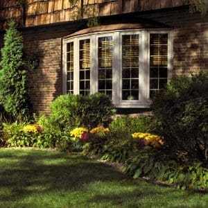 Exterior of residence featuring shrubbery, brick walls, and white bow windows.